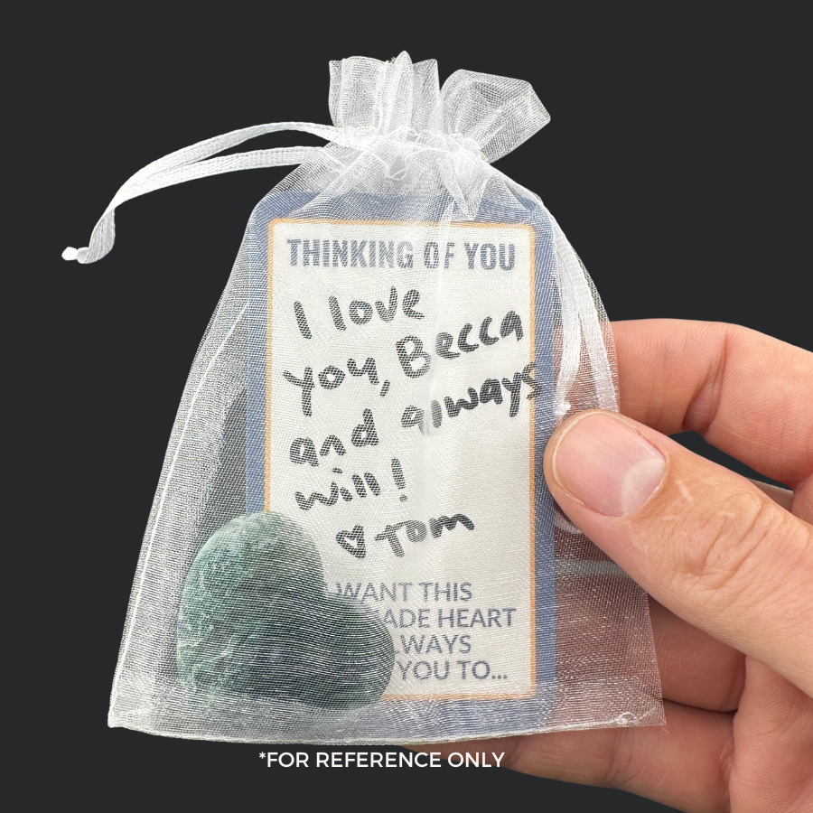 A heart-shaped stone with a handwritten Affirmations Card in a white gift bag.